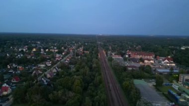 Alacakaranlıkta küçük bir köy ve ormandan geçen tren, hava manzaralı. panorama genel görünüm dronu 