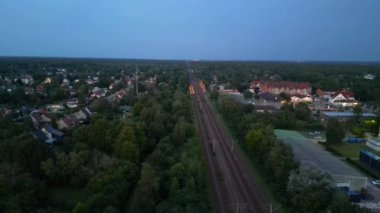 Alacakaranlıkta küçük bir köy ve ormandan geçen tren, hava manzaralı. panorama yörünge dronu 