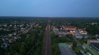 Alacakaranlıkta küçük bir köy ve ormandan geçen tren, hava manzaralı. uçuş üstü insansız hava aracı 