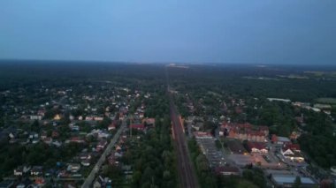Alacakaranlıkta küçük bir köy ve ormandan geçen tren, hava manzaralı. Yukarıdan insansız hava aracı görüntüleri 
