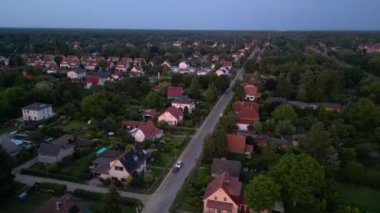 Brandenburg, Almanya 'da sakin bir akşam, çatıların, yemyeşil otlakların ve bir yol ağının sergilendiği bir yerleşim alanına iniyor. geniş yörünge görünümü dronu 