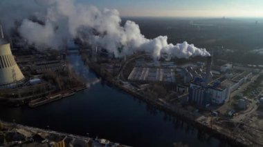 Endüstriyel bacalar mavi gökyüzünün altında beyaz duman yayıyor, kirlilik kavramı. İHA kamerası aşağıya bakıyor 