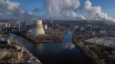 Nehir kenarındaki soğutma kulesinden buhar çıkaran ve şehir manzarasına bakan bir enerji santralinin hava görüntüsü. Sağ drona döndür 