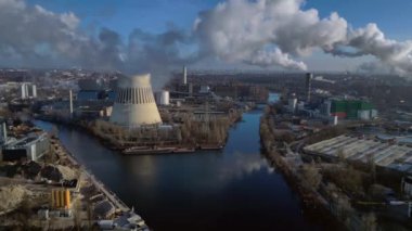 Nehir kenarındaki soğutma kulesinden buhar çıkaran ve şehir manzarasına bakan bir enerji santralinin hava görüntüsü. Yukarıdan insansız hava aracı görüntüleri 