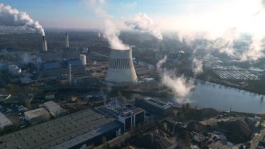 Nehir kenarındaki soğutma kulesinden buhar çıkaran ve şehir manzarasına bakan bir enerji santralinin hava görüntüsü. Yukarıdan insansız hava aracı görüntüleri 