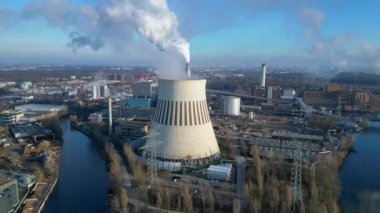 Güneşli bir günde, arka planda bir nehir ve şehir bulunan bir termik santralin dumanı yayan hava görüntüsü. statik üç ayaklı insansız hava aracı 