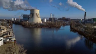 Nehir kenarındaki soğutma kulesinden buhar çıkaran ve şehir manzarasına bakan bir enerji santralinin hava görüntüsü. İHA alçalıyor 