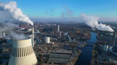 Güneşli bir günde, arka planda bir nehir ve şehir bulunan bir termik santralin dumanı yayan hava görüntüsü. Yukarıdan aşağıya doğru uçur 