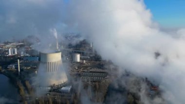 Güneşli bir günde, arka planda bir nehir ve şehir bulunan bir termik santralin dumanı yayan hava görüntüsü. Ters İHA uçuşu 