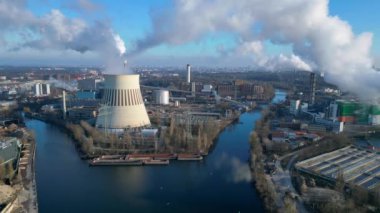 Güneşli bir günde, arka planda bir nehir ve şehir bulunan bir termik santralin dumanı yayan hava görüntüsü. panorama genel görünüm dronu 