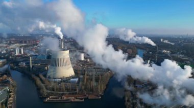 Güneşli bir günde, arka planda bir nehir ve şehir bulunan bir termik santralin dumanı yayan hava görüntüsü. statik üç ayaklı insansız hava aracı 