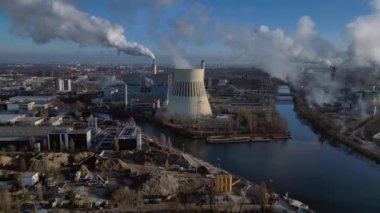 Nehir kenarındaki soğutma kulesinden buhar çıkaran ve şehir manzarasına bakan bir enerji santralinin hava görüntüsü. panorama genel görünüm dronu 
