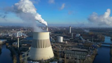 Nehir kenarındaki soğutma kulesinden buhar çıkaran ve şehir manzarasına bakan bir enerji santralinin hava görüntüsü. panorama genel görünüm dronu 