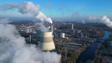 Güneşli bir günde, arka planda bir nehir ve şehir bulunan bir termik santralin dumanı yayan hava görüntüsü. uçuş üstü insansız hava aracı 