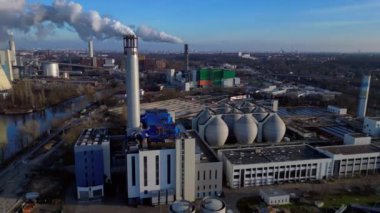 Atık atıkların enerji santraline uçarak bacasından çıkan dumanın kentsel bir alana yakın bir yere yayılması, atıkların çevresel etkileri. panorama yörünge dronu 