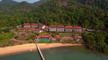 Tropikal bir adada deniz kenarında güzel bir tatil köyüne ulaşan uzun bir rıhtımın havadan görüntüsü. panorama genel görünüm dronu 