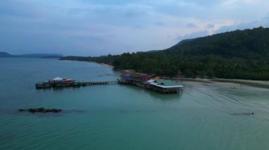 Koh Rong adası, bereketli palmiye ağaçları, canlı turkuaz suları ve geleneksel stilt evleriyle tropikal cennetin özünü yakalıyor. statik üç ayaklı insansız hava aracı 