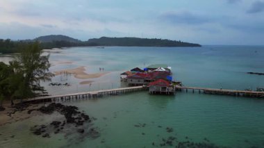 Koh Rong adası, bereketli palmiye ağaçları, canlı turkuaz suları ve geleneksel stilt evleriyle tropikal cennetin özünü yakalıyor. Yukarıdan insansız hava aracı görüntüleri 