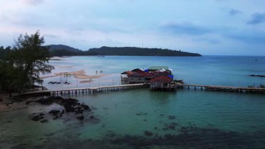 Koh Rong adası, bereketli palmiye ağaçları, canlı turkuaz suları ve geleneksel stilt evleriyle tropikal cennetin özünü yakalıyor. İHA alçalıyor 