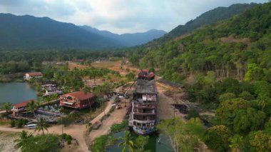 Tayland 'ın Koh Chang kentinde, palmiye ağaçları ve bir göl ile çevrili çürüyen binaları gösteren terk edilmiş bir tatil köyünün havadan görüntüsü. Dolly sol İHA 