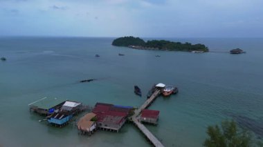 Koh Rong adası, bereketli palmiye ağaçları, canlı turkuaz suları ve geleneksel stilt evleriyle tropikal cennetin özünü yakalıyor. panorama genel görünüm dronu 
