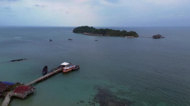 Koh Rong adası, bereketli palmiye ağaçları, canlı turkuaz suları ve geleneksel stilt evleriyle tropikal cennetin özünü yakalıyor. uçuş üstü insansız hava aracı 