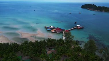 Koh Rong adası, bereketli palmiye ağaçları, canlı turkuaz suları ve geleneksel stilt evleriyle tropikal cennetin özünü yakalıyor. panorama yörünge dronu 