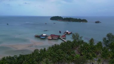 Koh Rong adası, bereketli palmiye ağaçları, canlı turkuaz suları ve geleneksel stilt evleriyle tropikal cennetin özünü yakalıyor. uçuş üstü insansız hava aracı 