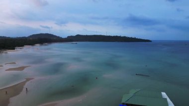 Koh Rong adası, bereketli palmiye ağaçları, canlı turkuaz suları ve geleneksel stilt evleriyle tropikal cennetin özünü yakalıyor. Ters İHA uçuşu 