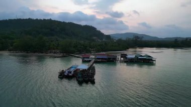Koh Rong adası, bereketli palmiye ağaçları, canlı turkuaz suları ve geleneksel stilt evleriyle tropikal cennetin özünü yakalıyor. panorama yörünge dronu 
