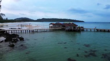 Koh Rong adası, bereketli palmiye ağaçları, canlı turkuaz suları ve geleneksel stilt evleriyle tropikal cennetin özünü yakalıyor. uçuş üstü insansız hava aracı 