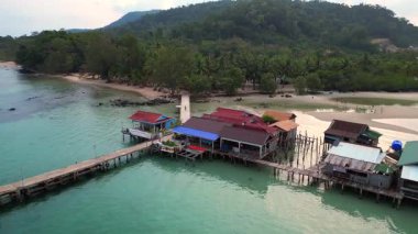 Koh Rong adası, bereketli palmiye ağaçları, canlı turkuaz suları ve geleneksel stilt evleriyle tropikal cennetin özünü yakalıyor. panorama yörünge dronu 