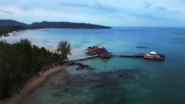 Koh Rong adası, bereketli palmiye ağaçları, canlı turkuaz suları ve geleneksel stilt evleriyle tropikal cennetin özünü yakalıyor. Drone görüntülerini daire içine al 