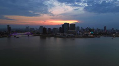 Phnom Penh ufuk çizgisi günbatımında Mekong nehrine renkli bulutlar ve arka planda bir köprüyle yansıyor. İHA alçalıyor 