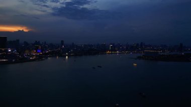 Phnom Penh ufuk çizgisi üzerinde gün batımı aydınlanmış bir köprüyle nehri geçmek ve yüzen tur tekneleriyle. Ters İHA uçuşu 