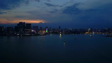 Phnom Penh ufuk çizgisi üzerinde gün batımı aydınlanmış bir köprüyle nehri geçmek ve yüzen tur tekneleriyle. Ters İHA uçuşu 