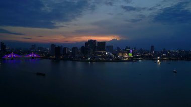 Phnom Penh ufuk çizgisi üzerinde gün batımı aydınlanmış bir köprüyle nehri geçmek ve yüzen tur tekneleriyle. Yukarıdan insansız hava aracı görüntüleri 