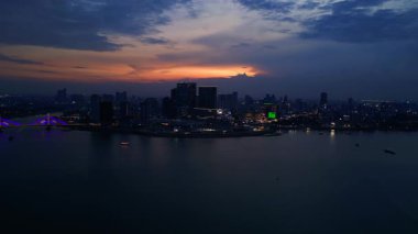 Phnom Penh ufuk çizgisi üzerinde gün batımı aydınlanmış bir köprüyle nehri geçmek ve yüzen tur tekneleriyle. panorama genel görünüm dronu 