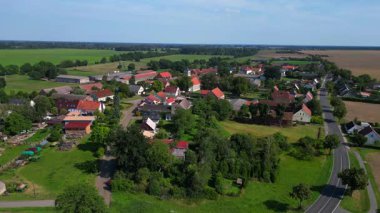 Almanya 'nın Brandenburg kentinde güneşli bir yaz gününde geniş tarım sahalarının ortasına kurulmuş küçük bir köy olan Tarmow' un Idyllic manzarası. panorama genel görünüm dronu 