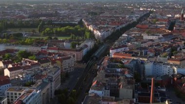 Berlin 'deki bir yerleşim bölgesinden geçen yükseltilmiş tren, şehrin taşıma sistemini gösteriyor. panorama yörünge dronu 