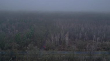 Karanlık ve kasvetli bir atmosferde sisli bir ormanın yakınındaki yolda araba sürüyordu. Yukarıdan insansız hava aracı görüntüleri 