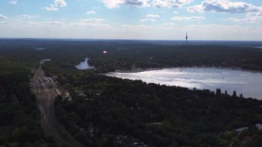 Wannsee göllerinde gezinen yelkenliler, güneşli bir günde, mavi gökyüzü ve bulutlarla çevrili yemyeşil ormanlarla çevrilidir. İHA alçalıyor 
