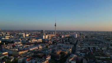 Berlin TV kulesi şehrin üzerinde dikiliyor, altın saatin sıcacık parıltısıyla yıkanıyor. Yukarıdan insansız hava aracı görüntüleri 