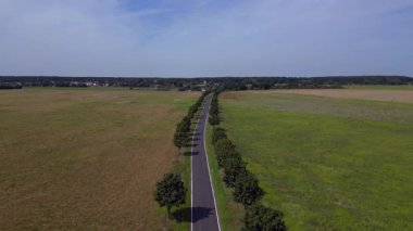 Ağaçlar ve tarlalarla dolu kırsal bir araziden geçen boş bir asfalt yolun havadan görünüşü. uçuş üstü insansız hava aracı 