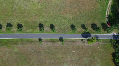 Ağaçlar ve tarlalarla dolu kırsal bir araziden geçen boş bir asfalt yolun havadan görünüşü. dikey kuş bakışı dron 