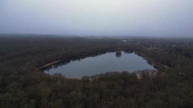 Göle bakan, ağaçlarla çevrili ve Almanya 'da bulutlu bir gökyüzünü yansıtan insansız hava aracı. Ters İHA uçuşu 
