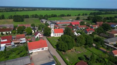 Almanya 'nın Brandenburg kentinde güneşli bir yaz gününde geniş tarım sahalarının ortasına kurulmuş küçük bir köy olan Tarmow' un Idyllic manzarası. panorama yörünge dronu 