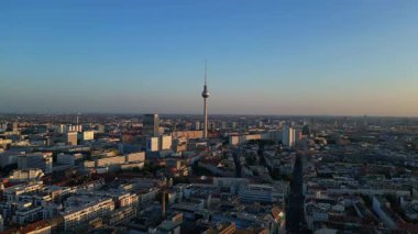 Berlin TV kulesi şehrin üzerinde dikiliyor, altın saatin sıcacık parıltısıyla yıkanıyor. Ters İHA uçuşu 