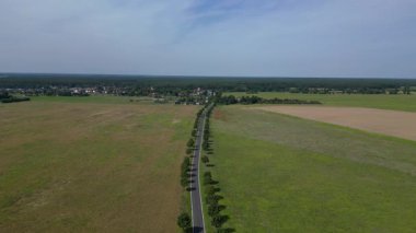 Ağaçlar ve tarlalarla dolu kırsal bir araziden geçen boş bir asfalt yolun havadan görünüşü. Yukarıdan insansız hava aracı görüntüleri 