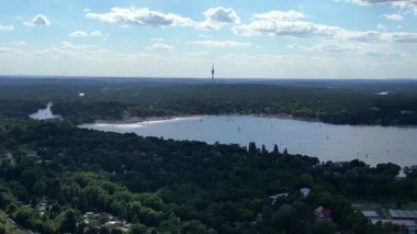 Wannsee göllerinde gezinen yelkenliler, güneşli bir günde, mavi gökyüzü ve bulutlarla çevrili yemyeşil ormanlarla çevrilidir. Sağ drona döndür 